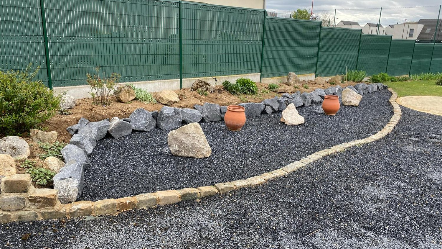 Massif aménagé en rocaille avec galets, plantes et allée gravier
